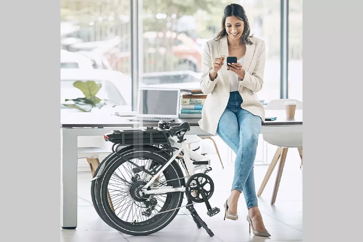 Woman next to a folded white Legend eBike in an office, illustrating the Fietslease / Fietsplan scheme in Belgium